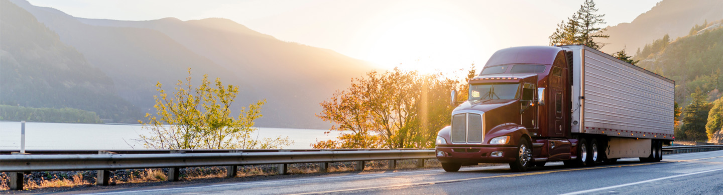 A truck moving from right to left with the river flowing in the middle ground and mountains in the background during early morning.